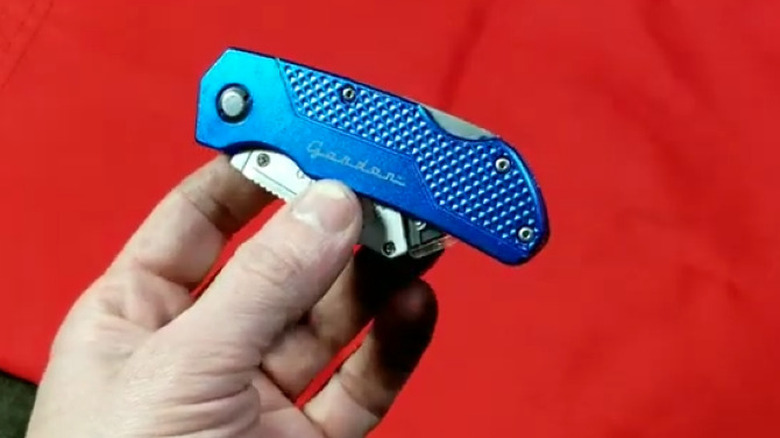Person holding a blue folding knife over red background