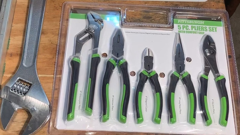 Set of pliers in plastic packaging on a table next to adjustable wrench