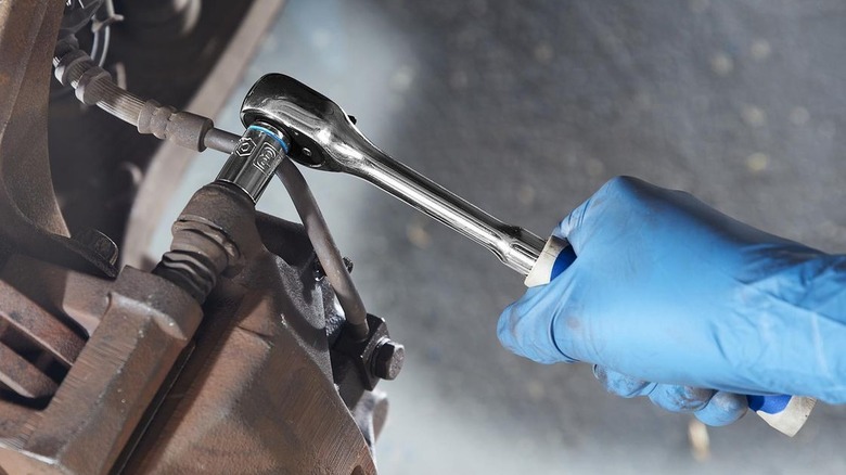 Person using ratchet to loosen brake caliper bolt