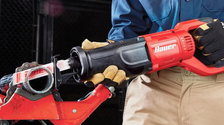 A person cuts a plastic tube with Bauer reciprocating saw.