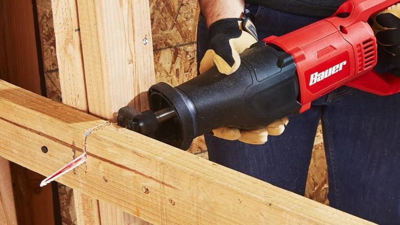 A person using a Bauer reciprocating saw to cut wood.