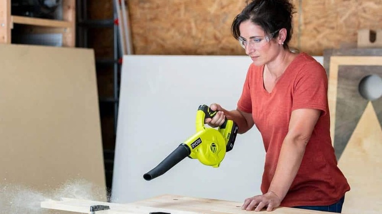 A woman blowing sand off of a piece of wood.