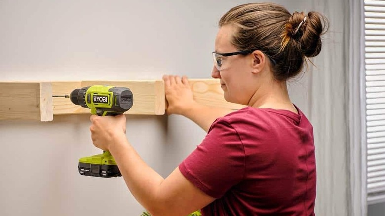 A woman drilling wood to a wall.