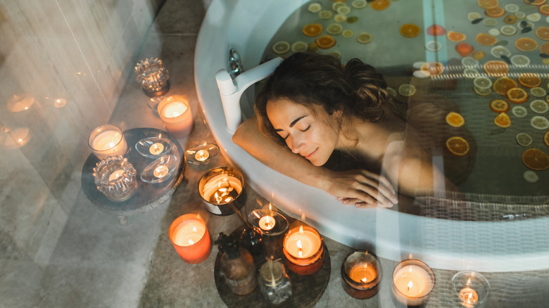 Woman in a large bathtub surrounded by candles