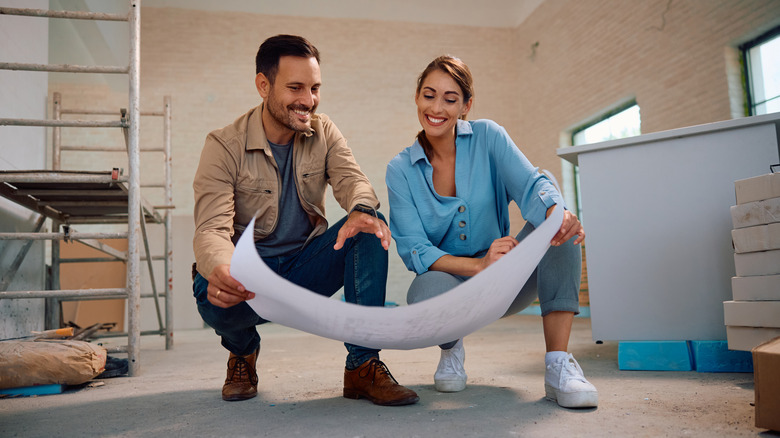 A couple examining home renovation blueprints in a room that's under construction