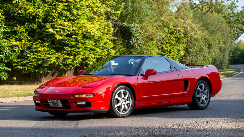 A red honda NSX parked in the shade on the side of a road, left two-quarters view visible
