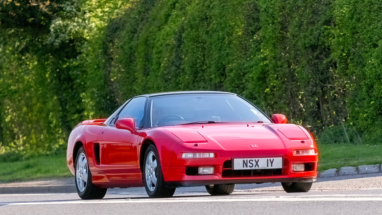 A gorgeous red Hona NSX seen parked on a road with shrubbery in the background