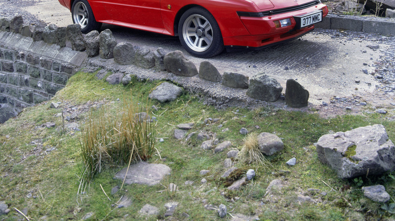 A red Mitsubishi Starion (or Chrysler Conquest) pictured parked on a rocky road on the side of a hill.