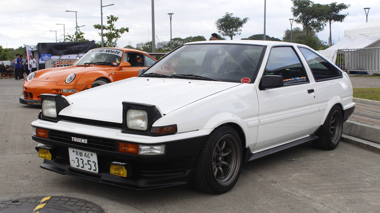 A white Toyota Trueno AE86 Corolla being displayed at a car show