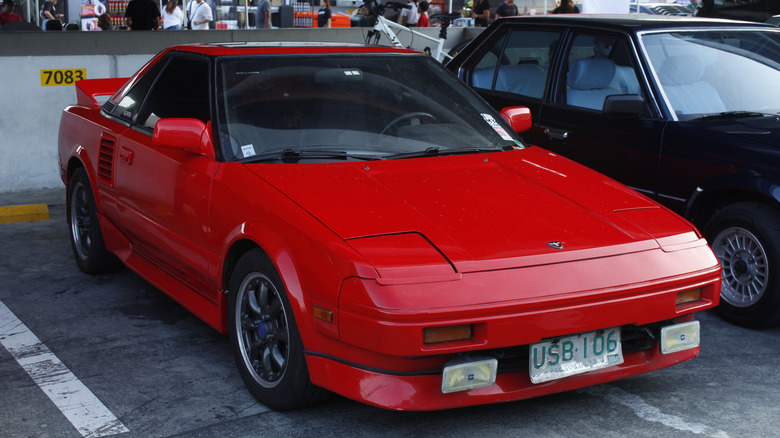 A classic red Toyota MR2 (mk1 generation) parked somewhere in the UK.