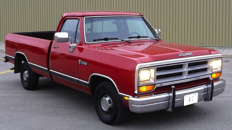 Front-side view of a red first-generation Dodge Ram pickup truck with headlights on.