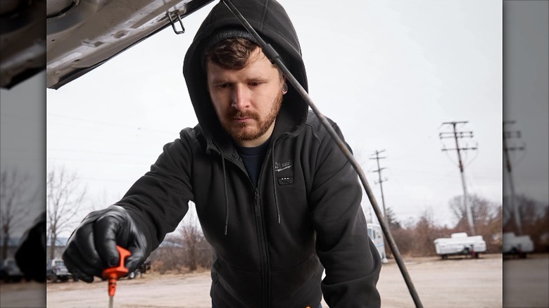 Man wearing a black heated hoodie outdoors to work on a car.