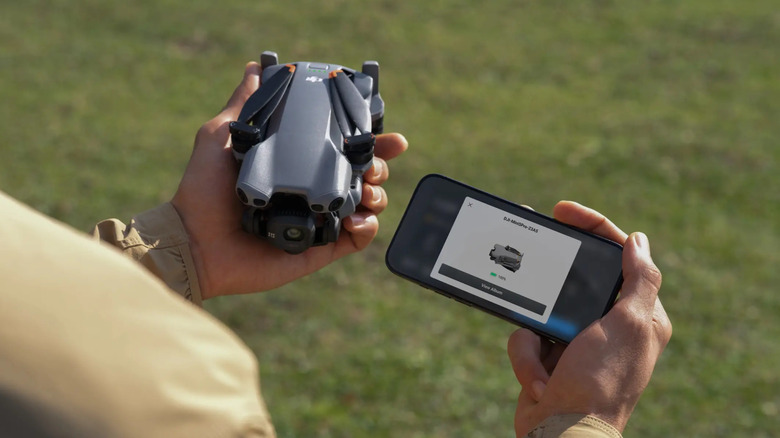 A person holding the DJI Mini5 Pro alongside their smartphone, outside