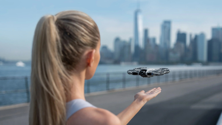 A woman holding her hand under the DJI Neo 2 outside, cityscape background