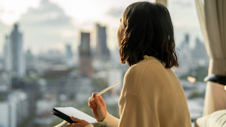 A woman with a tablet and a pencil looking out at a city skyline