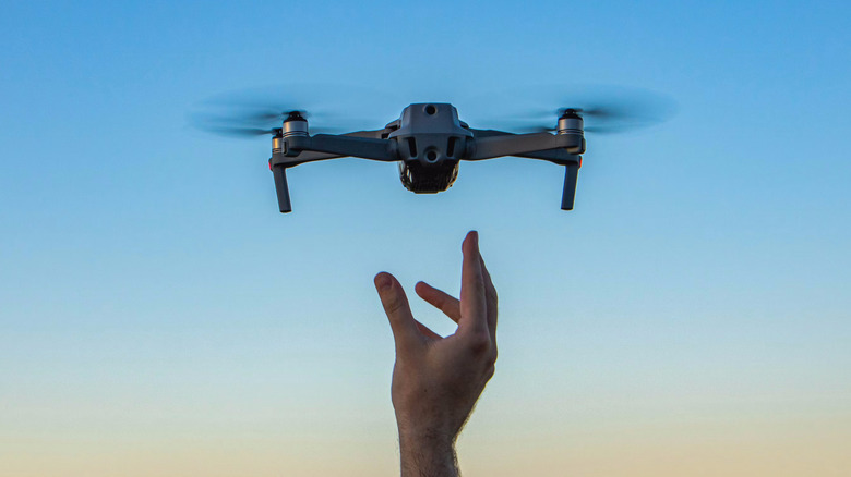 A drone flying in the sky with a hand reaching up for it