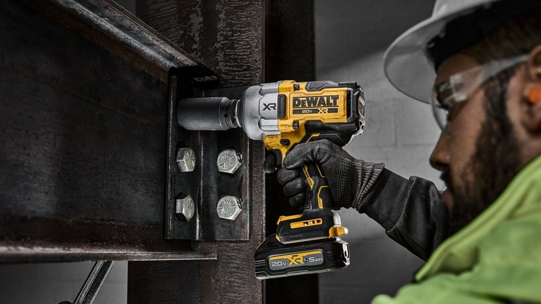 Construction worker using a Dewalt 20v Max XR cordless impact wrench to tighten large bolts on a steel beam.