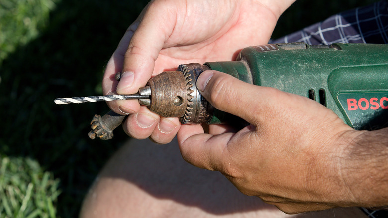 A person holding a green drill with two hands, in the process of changing the drill bit.