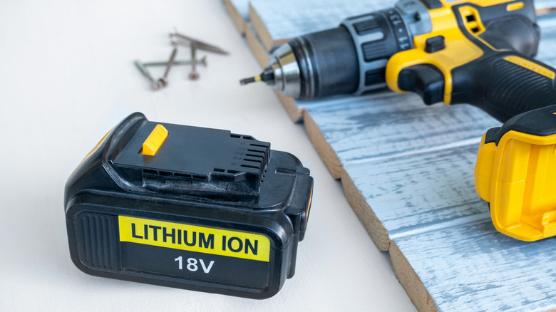 A yellow and black power tool battery sitting on a table near a matching drill.