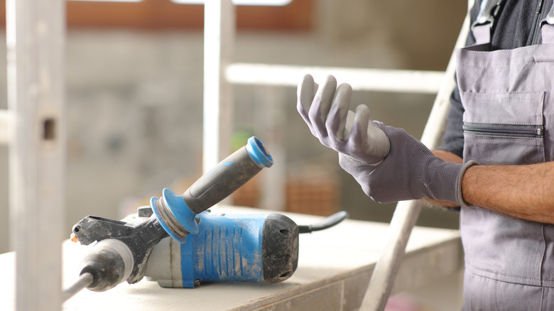A close up of a construction worker holding their wrist after using a power tool for a project.