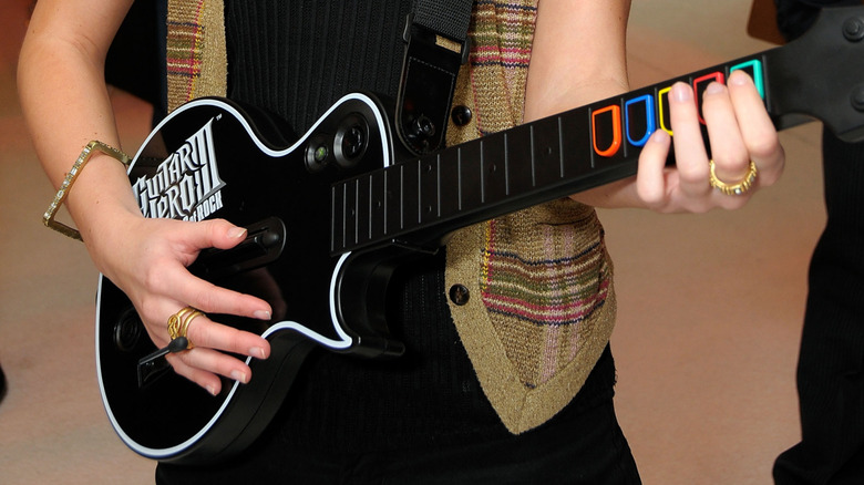A person holding the black Gibson Les Paul controller from "Guitar Hero III: Legends of Rock".