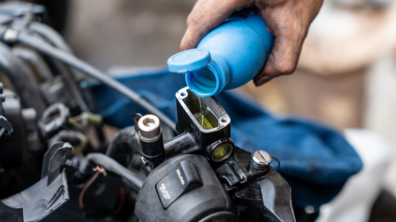 A mechanic adding brake fluid to a motorcycle's fluid reservoir