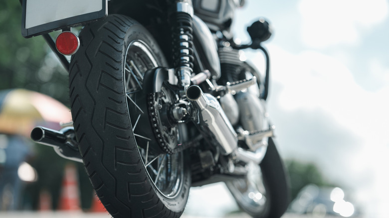 Close-up of a motorbike parked by the road, its rearr wheel and dual exhaust pipes visible