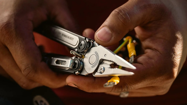 A pair of hands holding the Leatherman Arc multitool, along with some wires