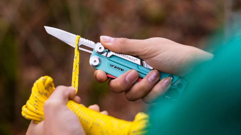 A person using the blade of a Leatherman Signal multitool to cut a yellow cord