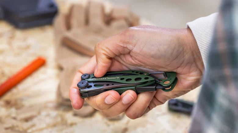 A person holding a green Leatherman Skeletool CX multitool