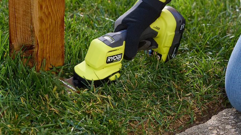 cutting grass near a post with Ryobi shears