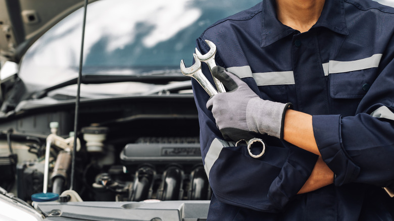 A mechanic holding two wrenches near a car
