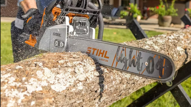 Person cutting through log with chainsaw