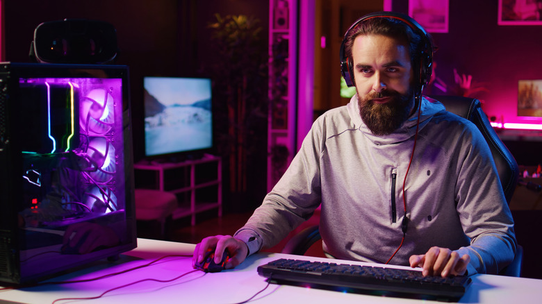 A person gaming with a smirk on their face, using a wired mouse and keyboard next to a computer