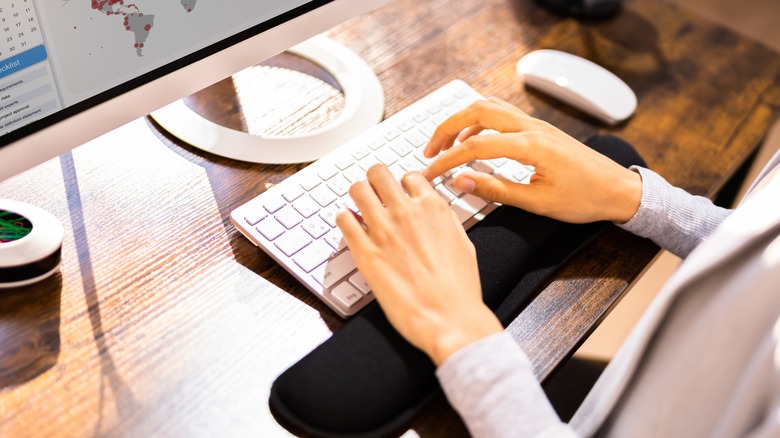 Woman typing on a white keyboard with a black wrist rest 