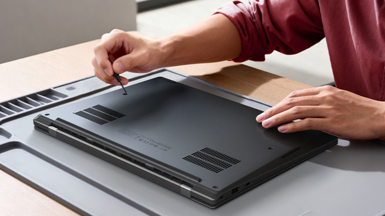 A man unscrews the bottom panel of the ThinkPad X1 Carbon Gen 14, revealing its user-accessible internals.
