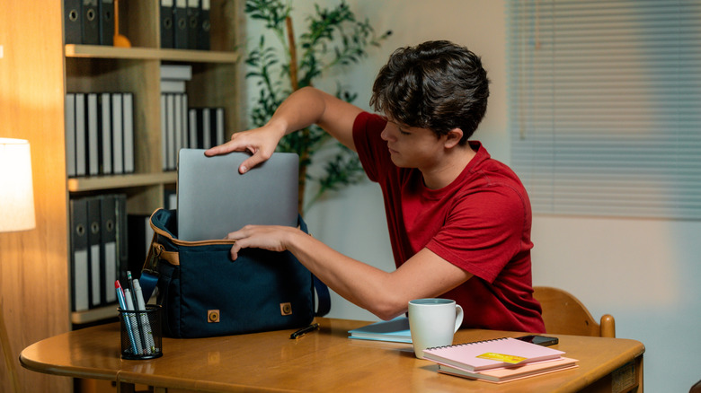 A student putting his laptop into a bag.