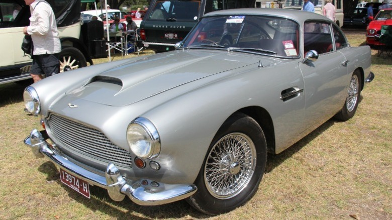 Silver Aston Martin DB4 parked on grass at a car show