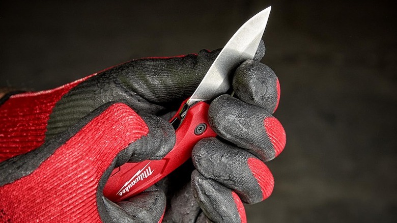 Holding a Milwaukee folding knife while wearing safety gloves.