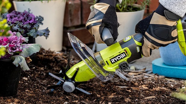 Person using a Ryobi 18V+ One Compact Cultivator to loosen soil