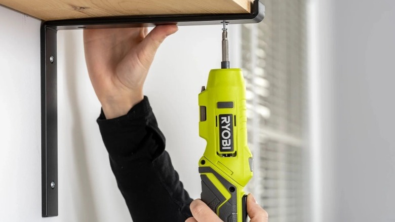 Person using the Ryobi USB Lithium Screwdriver to assemble wall-mounted shelving