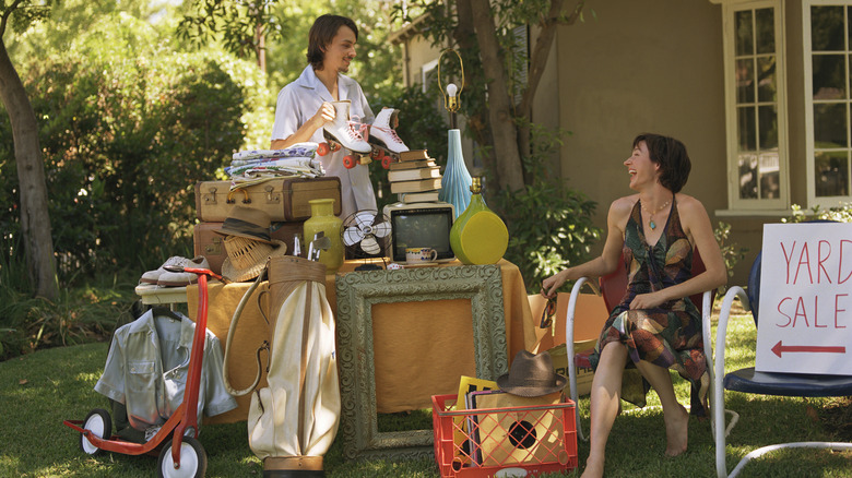 man holding up rollerskates and looking at a woman at a yard sale