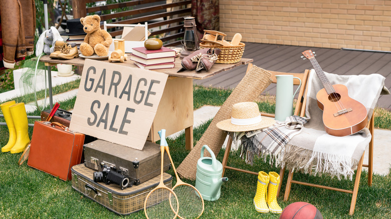 cardboard garage sale sign with many items out on yard