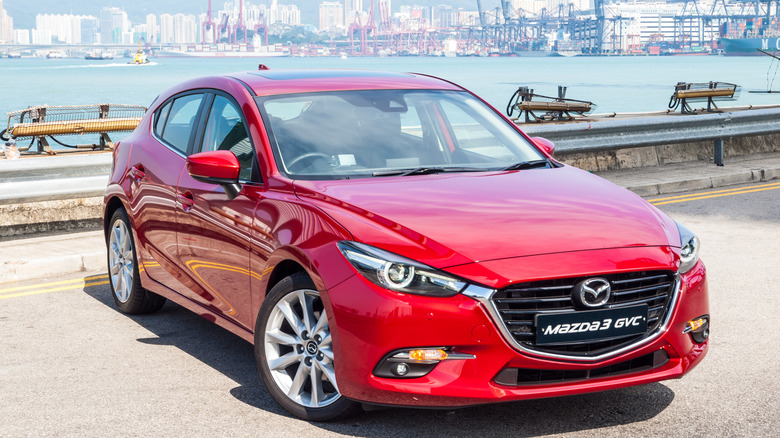red Mazda3 hatchback in front of a port