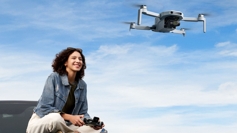 Person sitting on car hood while piloting Potensic Atom 2 drone.