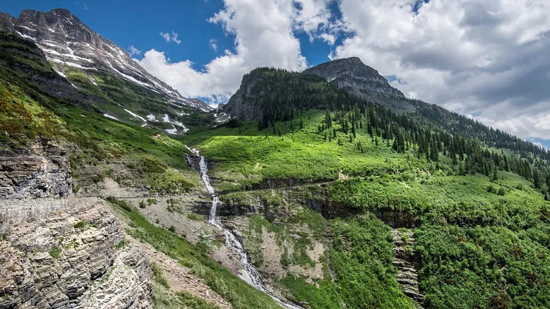 Scenic view of Going-to-the-Sun Road in Glacier National Park, Montana, with a narrow mountain road winding alongside cliffs and lush, green slopes.