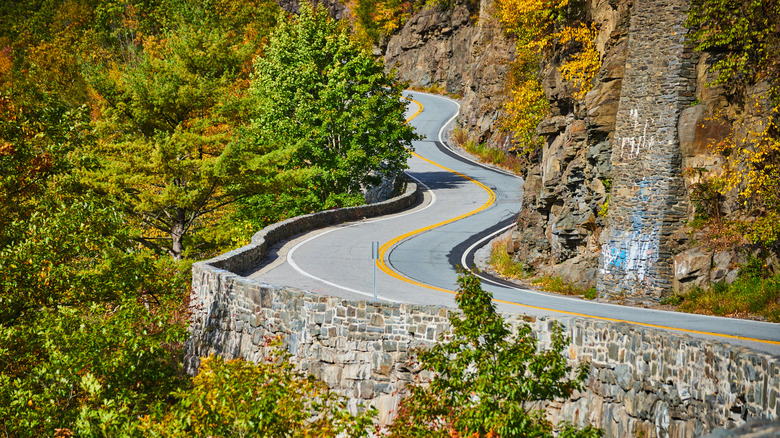 Winding cliffside road at Hawk's Nest in New York, curving sharply alongside stone walls and rugged rock faces.