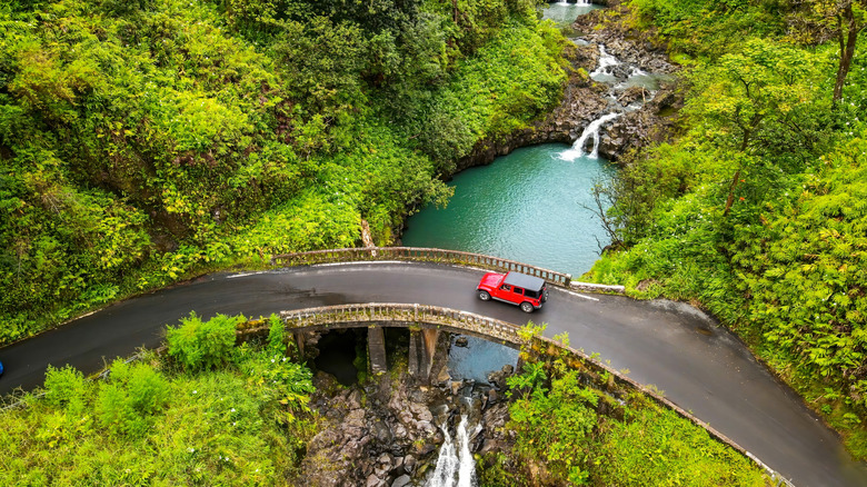 A red SUV crossing a narrow one-lane bridge on the Road to Hana in Maui, Hawaii.