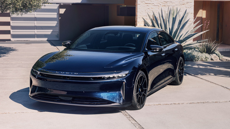 Blue Lucid Air Sapphire sedan seen from left front against a Southwest-looking building in background