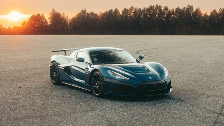 Blue Rimac Nevera seen from right front slightly elevated view with woods and sunset in background
